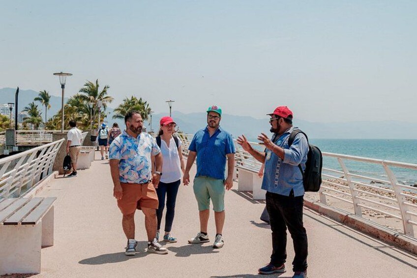 A coastal walkway with people walking, palm trees, and the sea in the background. 4