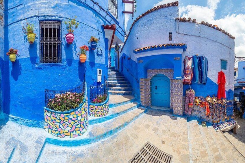 A narrow street with blue-painted buildings, a blue door, and colorful hanging plants. 3