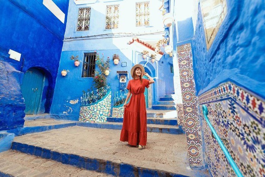 A person in a red dress standing on a staircase in a blue-painted alleyway with intricate tile work. 1