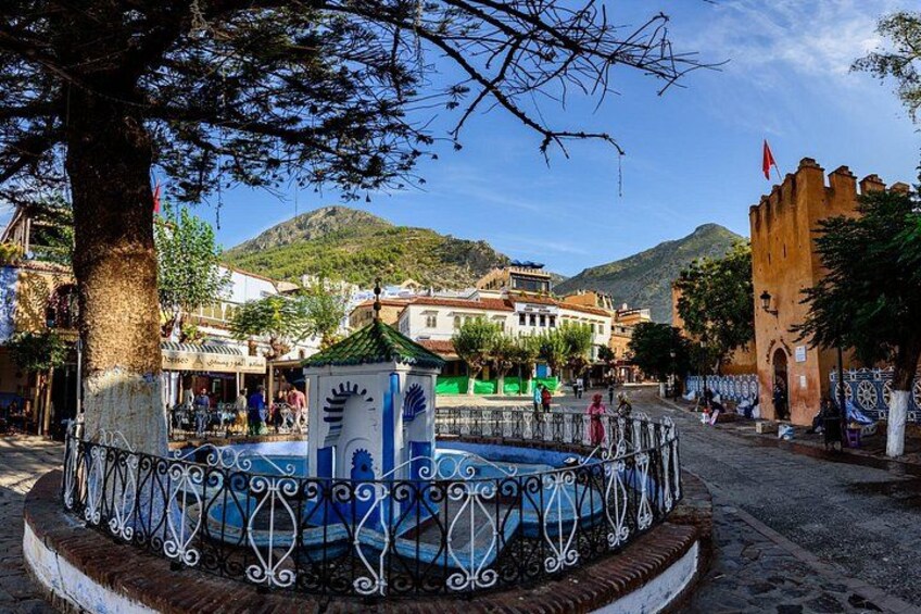 A town square with a fountain, a tree, and buildings in the background. 5