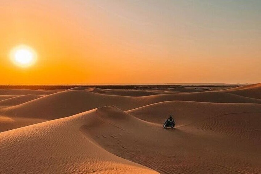 A motorcycle in a desert with sand dunes and a setting sun. 1
