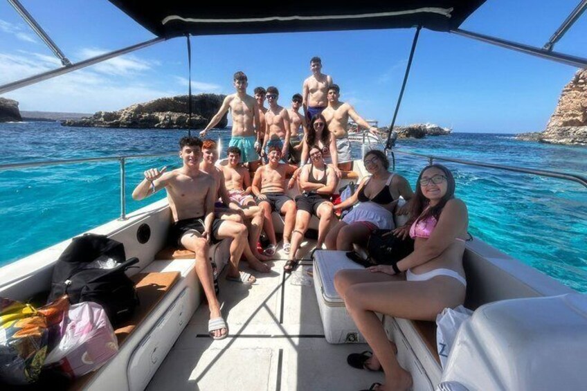 A group of people on a boat with clear blue water and rocky cliffs in the background. 4