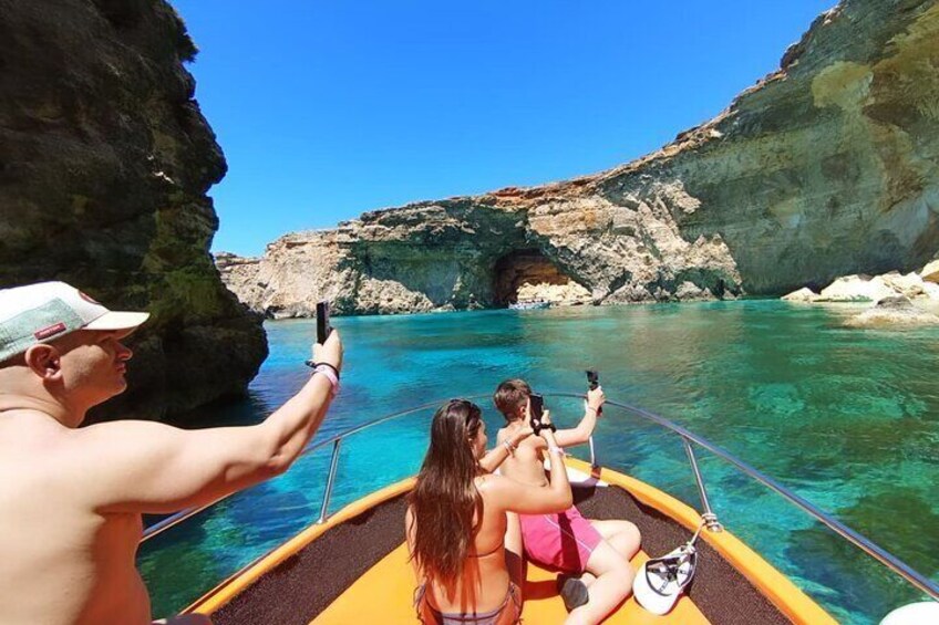 A boat tour with people taking photos of the clear blue water and rocky cliffs. 5