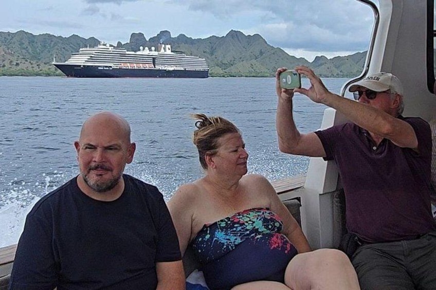 Three people on a boat with a cruise ship in the background and a mountainous landscape. 3
