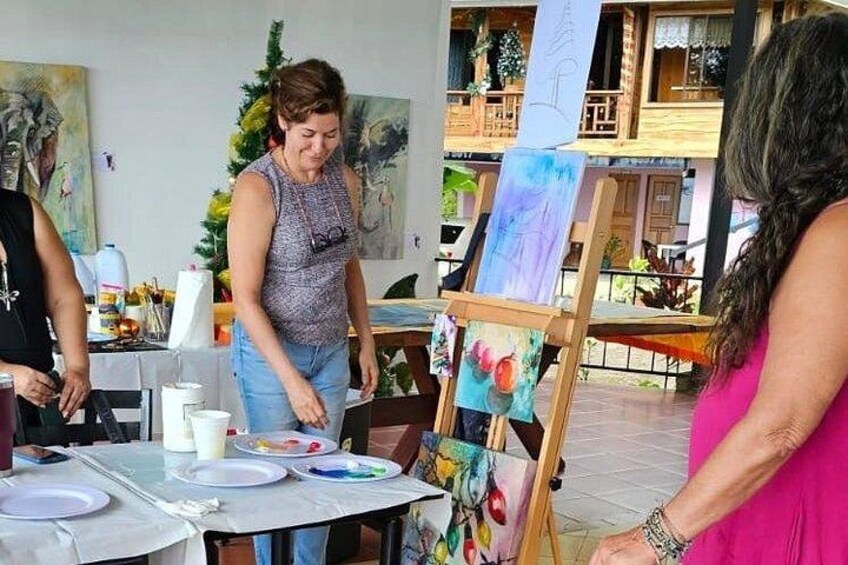 A person painting on an easel, a table with plates and cups, and a building with balconies in the background. 3
