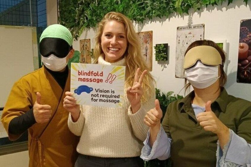 Drei Personen halten ein Schild, auf dem steht 'Blindmassagen' und 'Sehvermögen wird für die Massage nicht benötigt'. 3