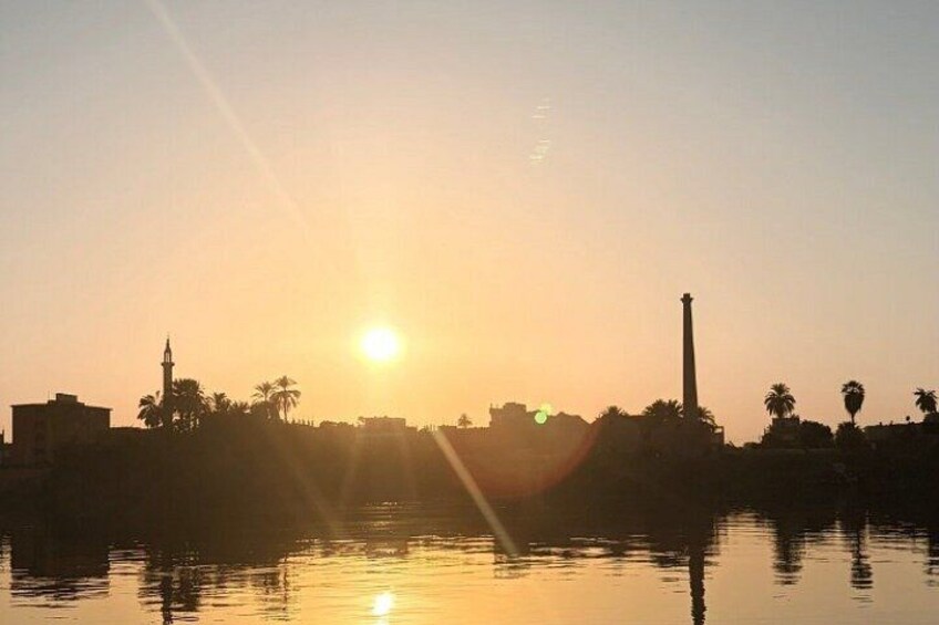 A sunset over a body of water with buildings and palm trees silhouetted against the sky. 3