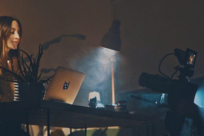Une personne assise à un bureau, avec un ordinateur portable, un appareil photo sur un trépied et une plante. 3