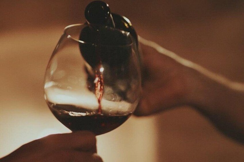 Une main tenant un verre à vin contenant un liquide sombre, vraisemblablement du vin, et un petit objet à l’intérieur. 4