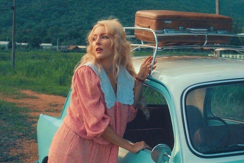 Une voiture ancienne, avec une valise posée sur le toit, garée dans un cadre rural. 1
