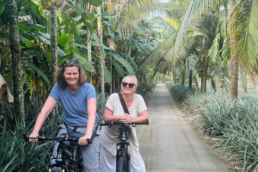 Two people on bicycles on a paved path surrounded by tropical vegetation. 2