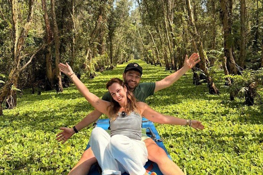 Two people on a blue raft in a forested area. 1