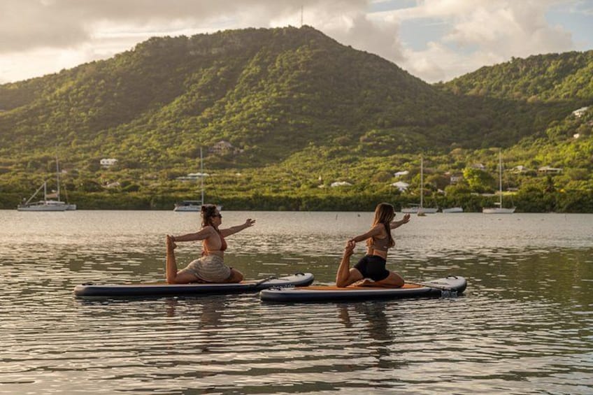 Two people practicing yoga on floating mats in a calm body of water with a mountainous landscape in the background. 4