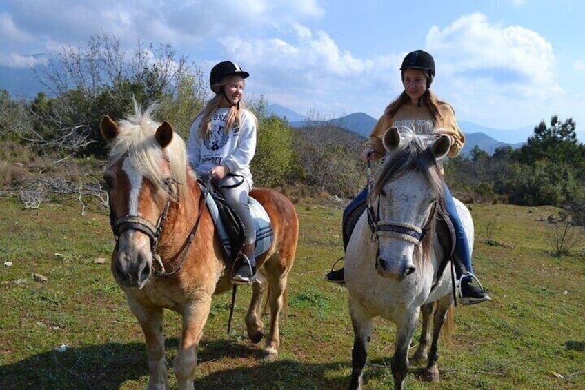 Zwei Personen reiten Pferde durch ein grünes Feld mit Bergen im Hintergrund. 1