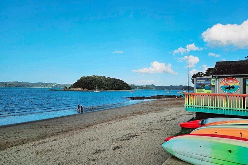A beach with a lifeguard tower, a small island in the distance, and colorful surfboards. 5