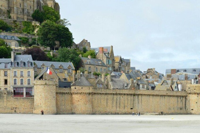 A historic stone wall with a flag, a castle, and buildings on a hill. 5