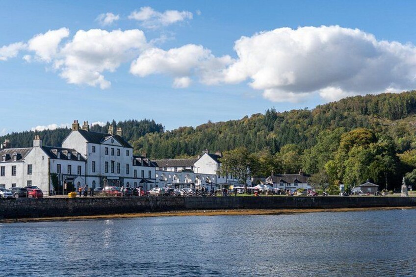 A waterfront town with buildings, a clear sky, and a forested hill in the background. 4