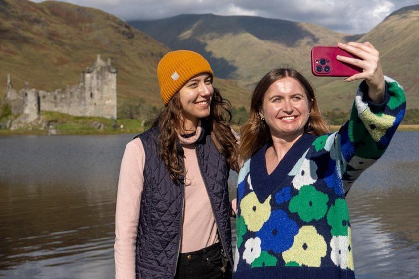 Two people taking a selfie with a castle and mountains in the background. 1