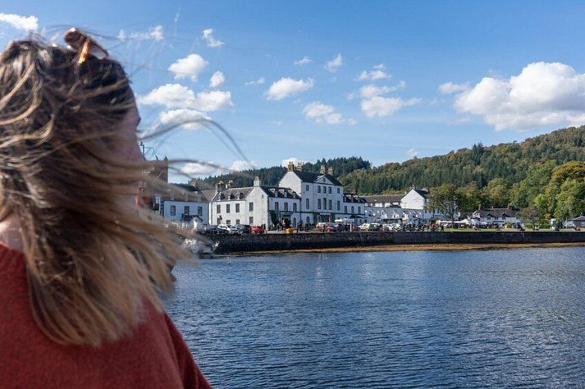 A waterfront view with a large white building, calm water, and a forested hill in the background. 3