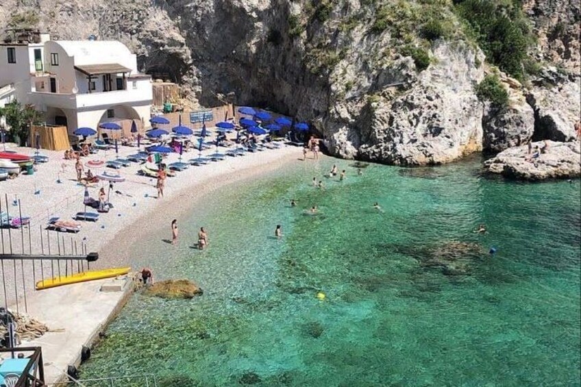 A coastal beach with clear water, umbrellas, and people swimming. 3