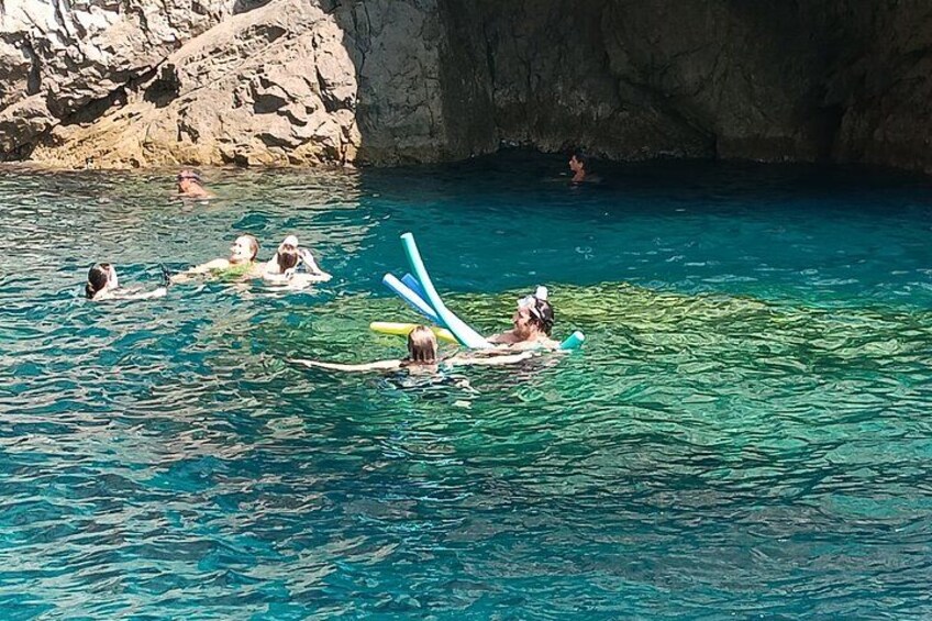 People swimming and floating in a clear blue pool with rocky cliffs in the background. 2