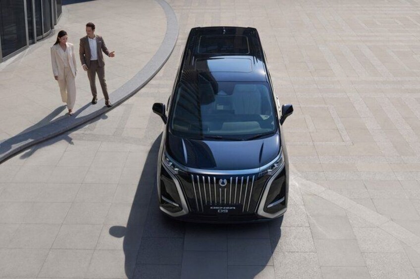 A modern car parked on a paved surface with two people walking nearby. 5
