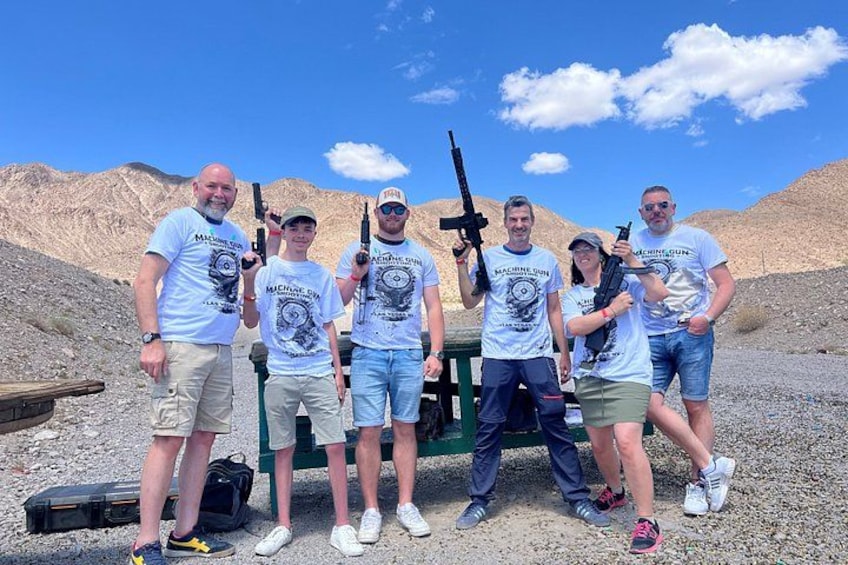 A group of people in a desert setting with rifles, a green structure, and a clear sky. 4