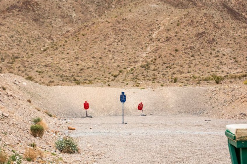 A barren landscape with a shooting range, including targets and a green trash bin. 2