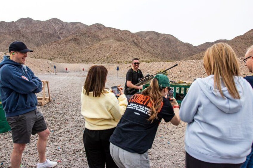 A group of people at an outdoor shooting range with targets in the distance. 3