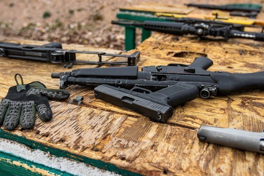 A wooden table with firearms, ammunition, and a pair of gloves. 5