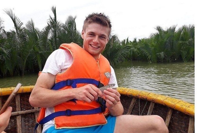 A person in a boat wearing an orange life jacket, holding a camera, with palm trees in the background. 3
