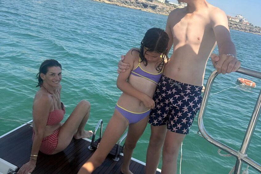 Three people on a boat with a rocky shoreline in the background. 3