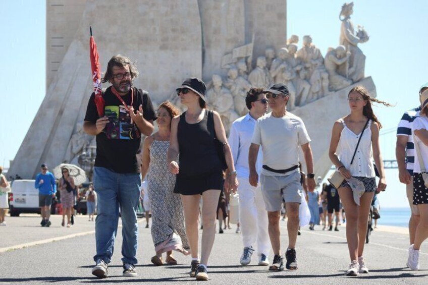 Un grupo de personas caminando por un paseo marítimo con una gran estatua al fondo. 1