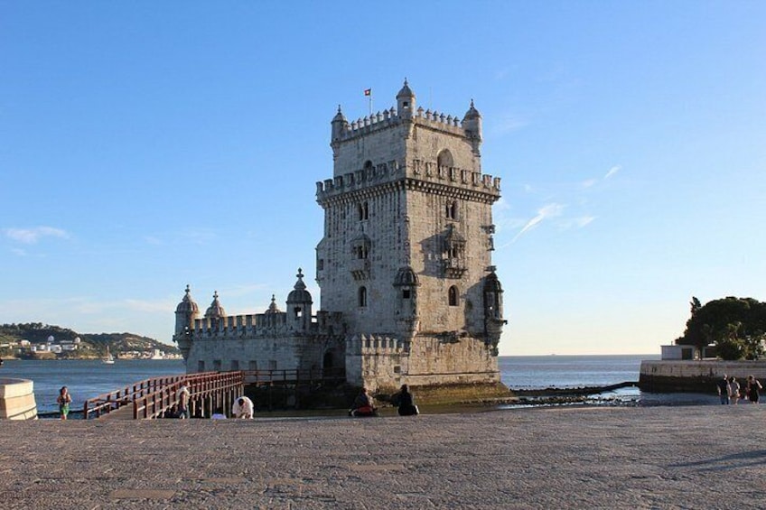 Una torre histórica junto al mar, un paseo empedrado y una costa distante. 5