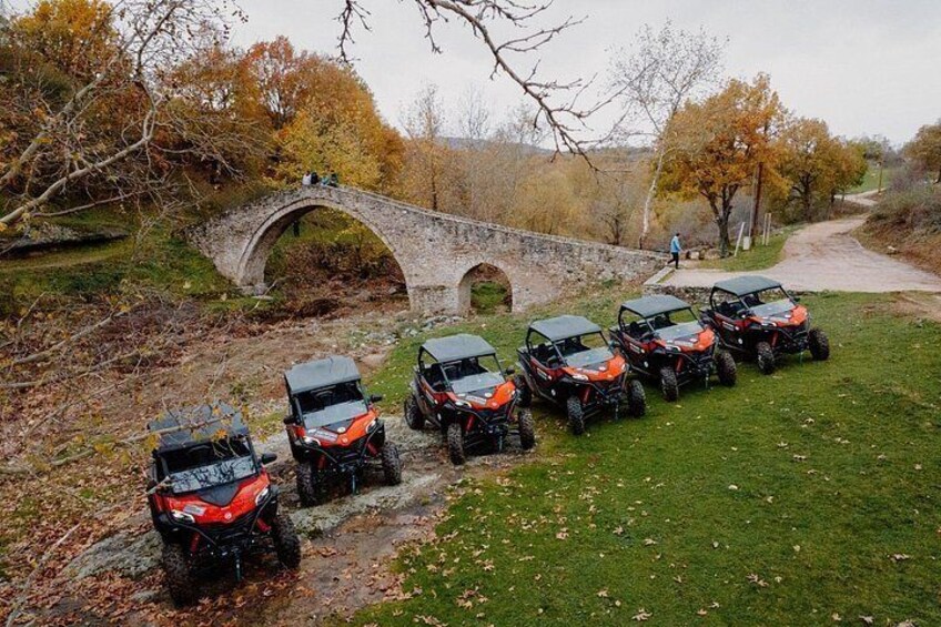 Eine Gruppe von Quads ist auf einem grasbewachsenen Pfad geparkt, im Hintergrund eine Steinbrücke. 1