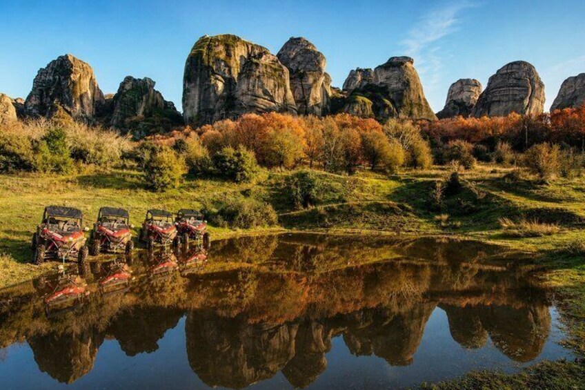 A group of off-road vehicles parked by a calm lake with rock formations in the background. 3