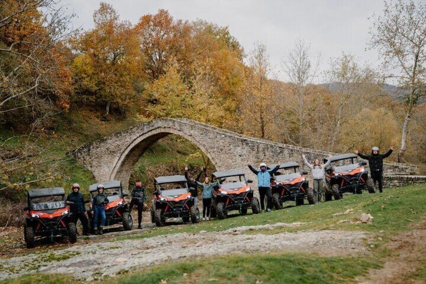A group of people with ATVs in front of a stone bridge in a wooded area. 4