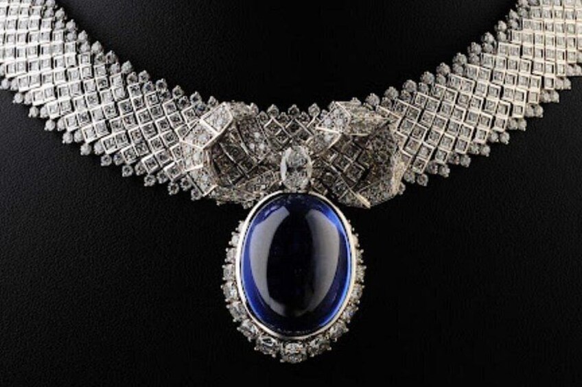Een collier met een grote blauwe steen als hanger en een zilveren ketting met een diamantpatroon. 2