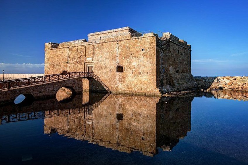 A stone fortress with a bridge, reflecting in calm water under a clear sky. 5