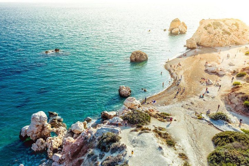 A coastal beach with clear turquoise water, rocky outcrops, and people sunbathing. 3
