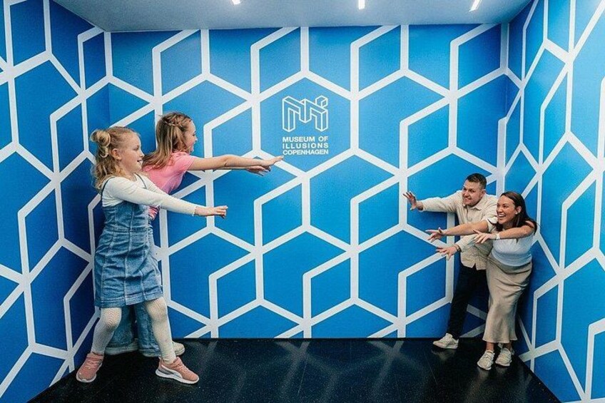 A group of people interacting with a blue geometric wall with a logo. 3