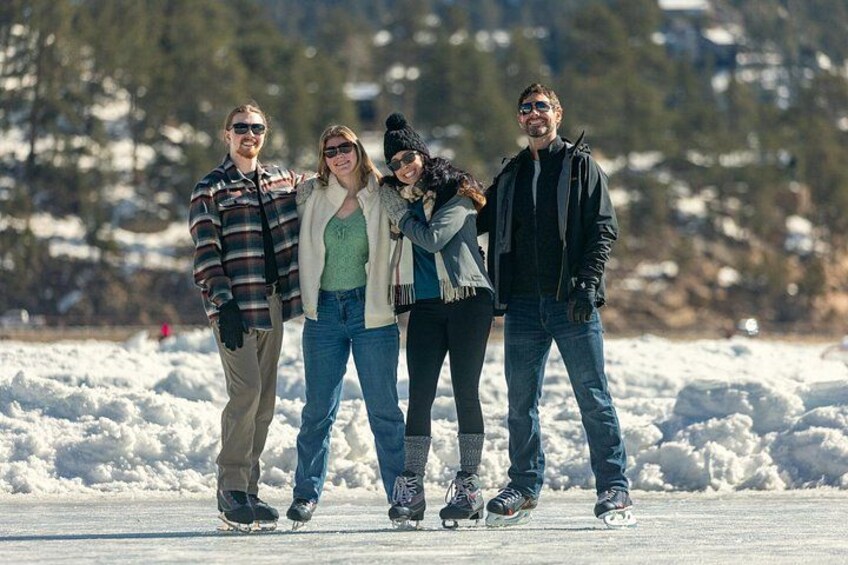 Four people ice skating on a frozen surface with snow-covered trees in the background. 4