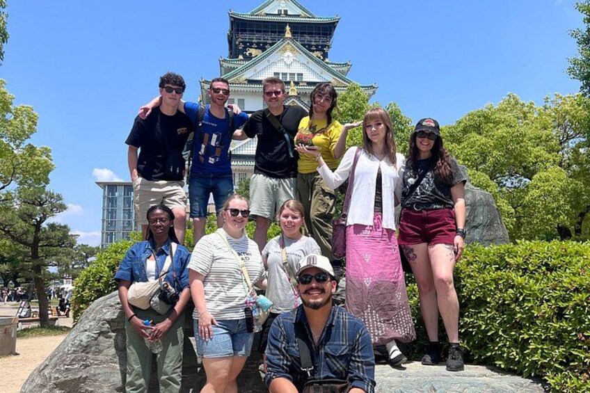 Un grupo de personas posando frente a un edificio tradicional japonés con techo verde y paredes blancas. 1