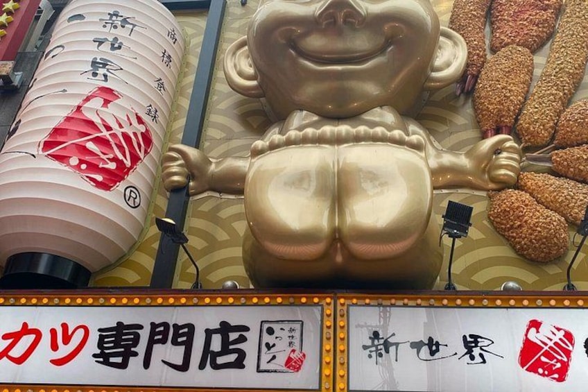 Un'ampia statua dorata raffigurante una figura sorridente, un tradizionale lanterne e un cartello con caratteri giapponesi. 2
