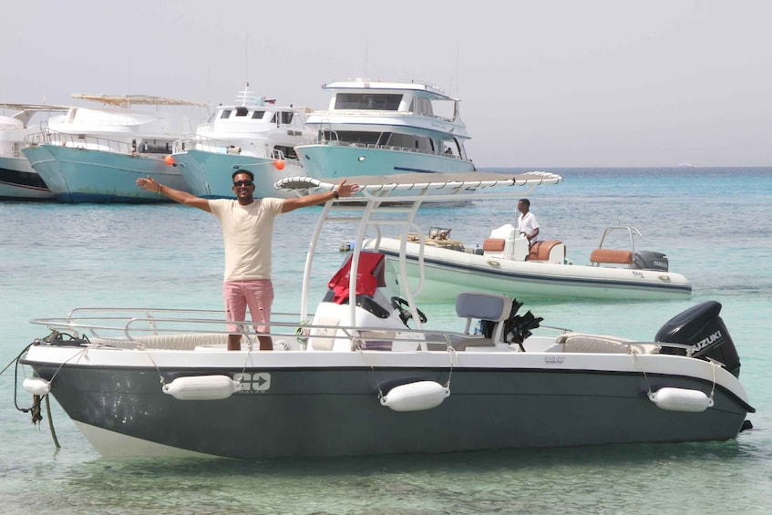 Un homme se tient debout sur un bateau, les bras tendus, un autre homme se trouve sur un bateau plus petit à proximité, et plusieurs bateaux plus grands sont visibles à l’arrière-plan. 5