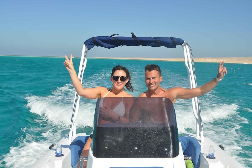 Deux personnes se trouvent sur un bateau, avec une mer d’un bleu éclatant et une plage de sable en arrière-plan. 2