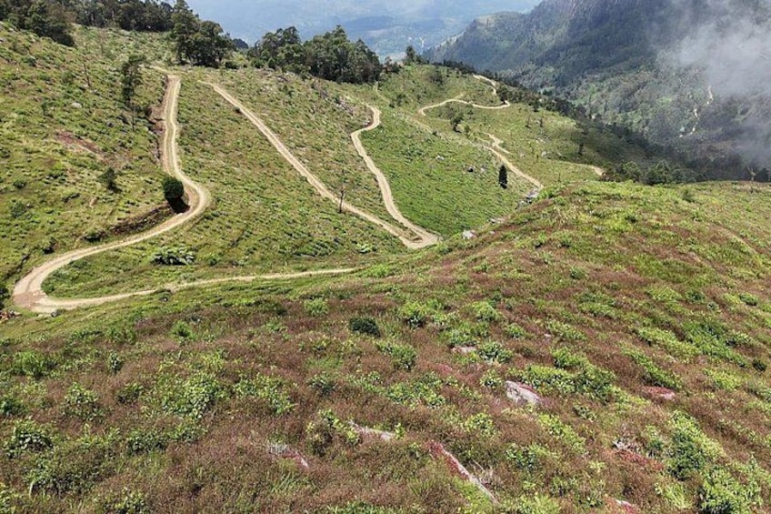A winding dirt road through a hilly landscape with patches of grass and shrubs. 2