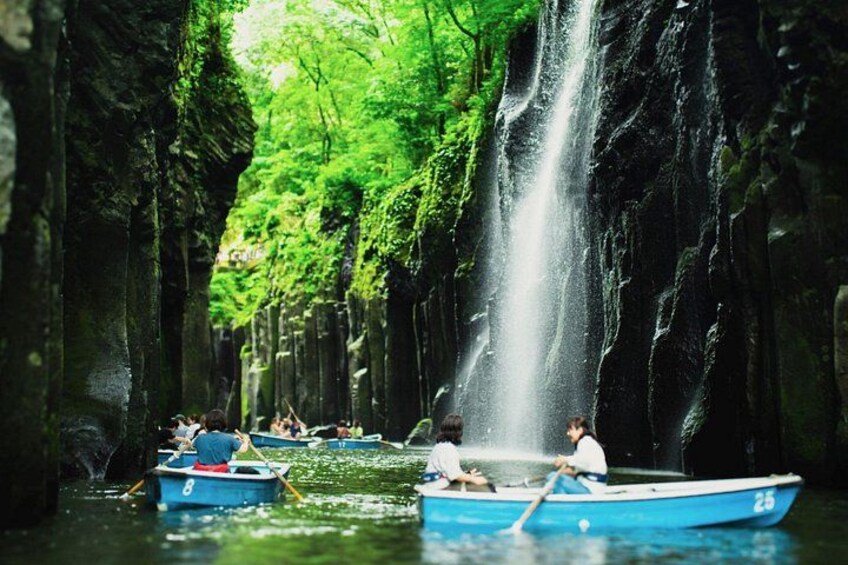 A waterfall in a forested area with people paddling boats. 1
