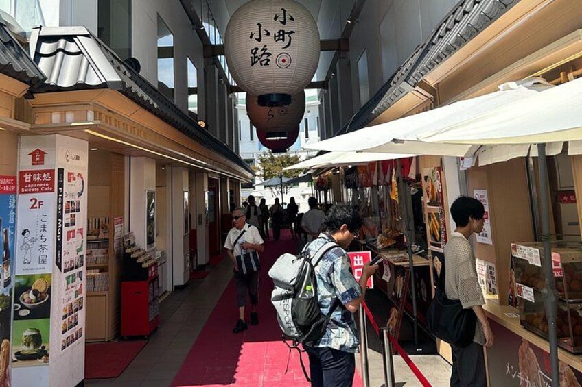 A narrow indoor corridor with shops on either side, a red carpet, and hanging lanterns. 1