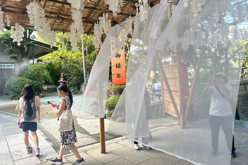 A covered outdoor area with hanging decorations, a sign with Japanese characters, and a person taking a photo. 4